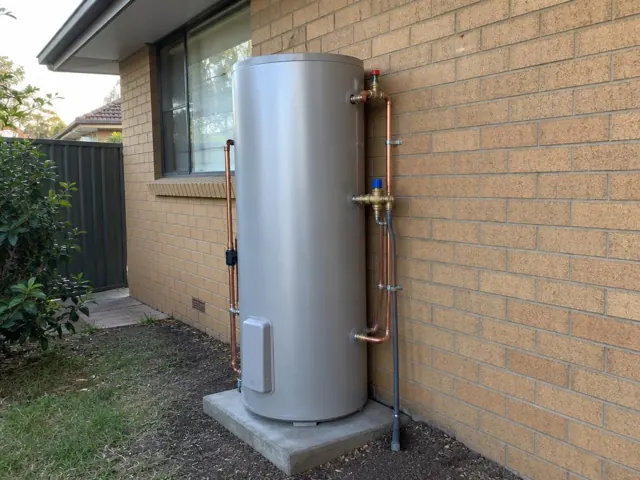 Outdoor hot water system on a concrete pad beside a brick house wall in Plumpton